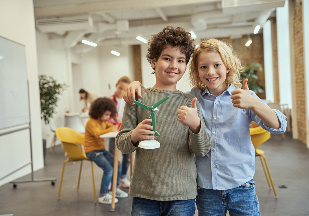 Portrait of two happy boys showing thumbs up while holding mechanical toy