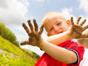 A Young Boy with muddy hands playing outside.