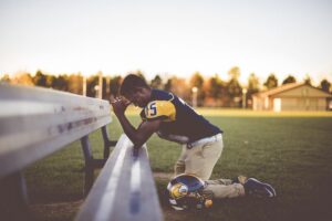 boy football player kneeling and praying at a field.